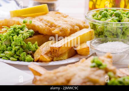 Britannico tradizionale cibo di strada pesce e patatine con fiacco piselli sul piatto di carta Foto Stock