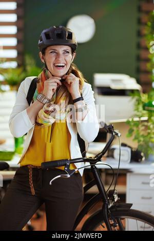 donna business sorridente moderna in casco con bicicletta in un moderno ufficio ecologico. Foto Stock