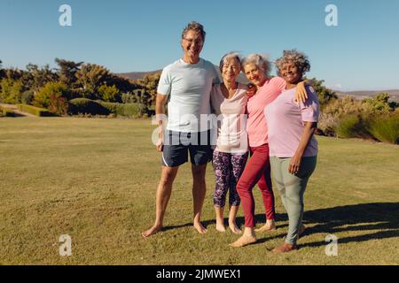 Ritratto di sorridenti amici senior multirazziali in piedi su terra erbosa contro cielo chiaro in cortile Foto Stock