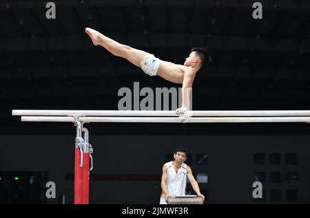 FUYANG, CINA - 7 AGOSTO 2022 - Un bambino pratica la ginnastica si muove sotto la guida di un allenatore alla palestra di Fuyang Vocational and Technical Foto Stock