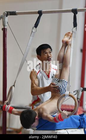 FUYANG, CINA - 7 AGOSTO 2022 - Un bambino pratica la ginnastica si muove sotto la guida di un allenatore alla palestra di Fuyang Vocational and Technical Foto Stock