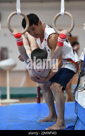 FUYANG, CINA - 7 AGOSTO 2022 - Un bambino pratica la ginnastica si muove sotto la guida di un allenatore alla palestra di Fuyang Vocational and Technical Foto Stock