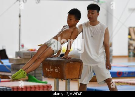 FUYANG, CINA - 7 AGOSTO 2022 - Un bambino pratica la ginnastica si muove sotto la guida di un allenatore alla palestra di Fuyang Vocational and Technical Foto Stock