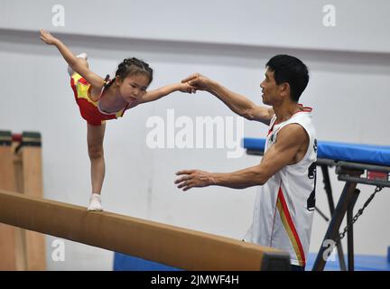 FUYANG, CINA - 7 AGOSTO 2022 - Un bambino pratica la ginnastica si muove sotto la guida di un allenatore alla palestra di Fuyang Vocational and Technical Foto Stock