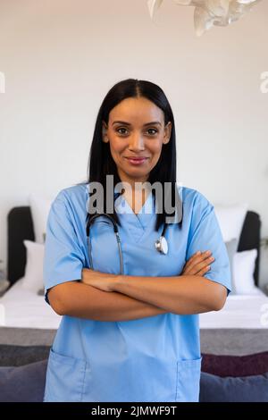 Ritratto di fidata fisioterapista biraciale femminile con le braccia incrociate in piedi a casa, copia spazio Foto Stock