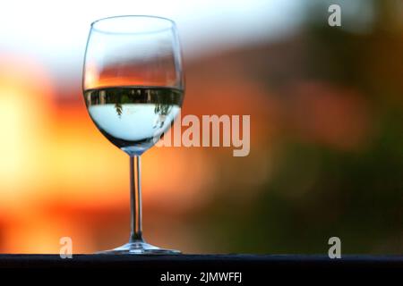 Bicchiere di vino bianco sullo sfondo sfocato del tramonto Foto Stock