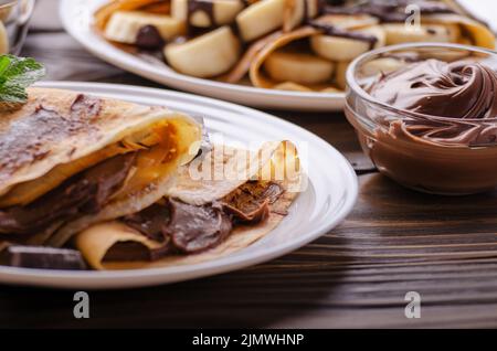 Il francese crepes con salsa di cioccolato e banana nel piatto di ceramica su legno tavolo da cucina Foto Stock