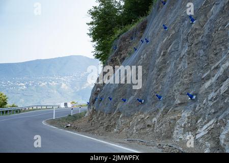 Prevenzione delle frane e dello scivolamento delle rocce in Georgia, rinforzando il pendio di montagna con rete metallica. Foto Stock