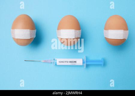 flatlay con siringa di vaccino di scimmietta e uova vaccinate con cerotto medico su sfondo blu. Foto Stock