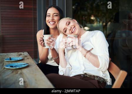 Tutto ciò di cui avete bisogno è un buon amico e un buon caffè. Due giovani donne che si divertono a vicenda mentre si sorseggiano un caffè in un bar. Foto Stock