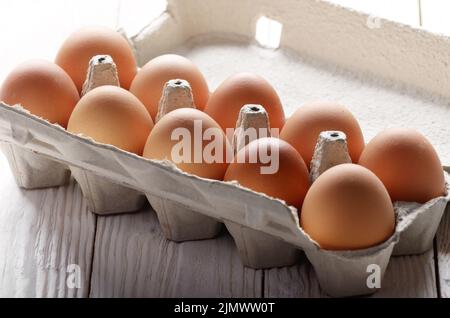 Materie organica marrone le uova di gallina in eco-friendly cartone carta sulla cucina bianca tavolo in legno Foto Stock