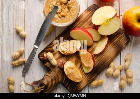 Appartamento con vista sul piano di taglio con fette di mela con burro di arachidi su tavolo da cucina in legno bianco Foto Stock