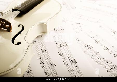 Chiudere la vista di un violino e note musicali su bianco tavolo in legno Foto Stock