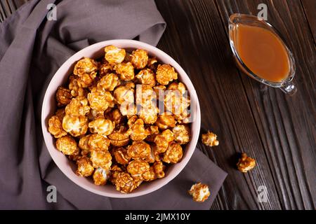 Ciotola di argilla con popcorn caramello su fondo di legno piatto Foto Stock