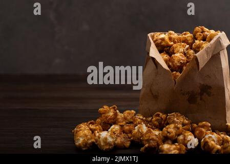 Popcorn caramellato in sacchetto di carta su tavolo da cucina in legno Foto Stock