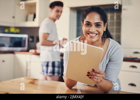 Theres sempre così tanto per mettersi in pari la mattina. Una giovane donna che usa un tablet digitale mentre il suo ragazzo si alza sullo sfondo. Foto Stock