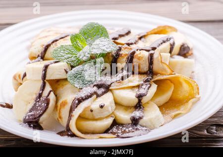 Il francese crepes con salsa di cioccolato e banana nel piatto di ceramica su legno tavolo da cucina Foto Stock