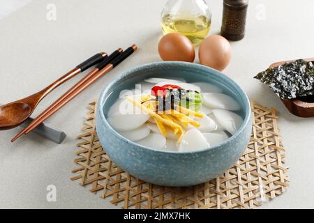 Zuppa di torta di slice coreana o Tteokguk su Blue Bowl. Condimento con uovo, peperoncino, alghe e cipolla primaverile. Zuppa popolare per la riunione della famiglia Foto Stock