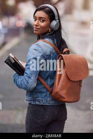 Oggi devi iniziare il tuo futuro: Una giovane donna che cammina per la città indossando le cuffie mentre trasporta i suoi libri. Foto Stock