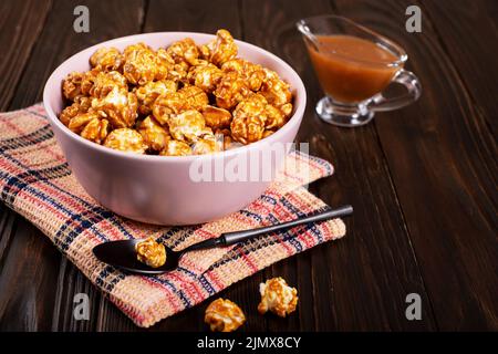 Ciotola in argilla con popcorn al caramello su sfondo di legno Foto Stock