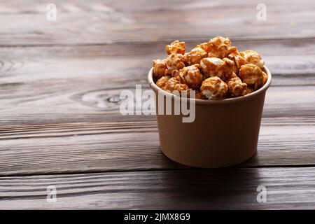 Popcorn caramellato in secchio di carta su tavolo da cucina in legno Foto Stock