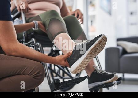 Facciamo il primo passo verso il recupero. Un fisioterapista irriconoscibile che fa esercizi alle gambe con la sua paziente legata alla sedia a rotelle all'interno del suo ufficio Foto Stock