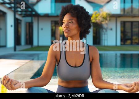 Giovane afro afroamericana che guarda via mentre pratichi lo yoga a bordo piscina Foto Stock