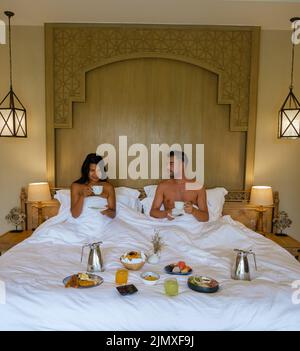 Coppia uomini e donne che hanno la colazione a letto, camera da letto di lusso con lampade di stile arabo e letto Foto Stock
