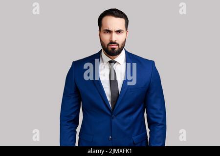 Ritratto di uomo d'affari bearded che guarda la macchina fotografica con il volto arrabbiato, avendo aggressivo espressione facciale, indossando il vestito di stile ufficiale. Studio interno girato isolato su sfondo grigio. Foto Stock