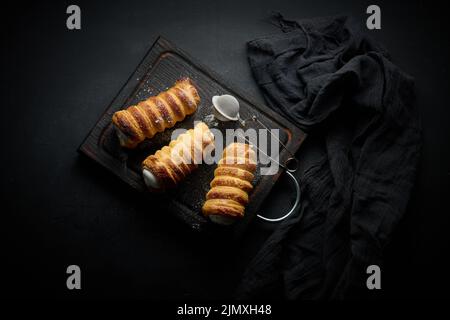 Tubuli al forno ripieni di panna montata su un tavolo da cucina in legno nero, vista dall'alto Foto Stock