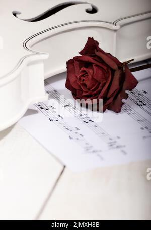 Chiudere la vista di un bianco secco di violino rosa e note musicali su un tavolo di legno Foto Stock