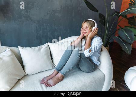 Bella ragazza giovane sul divano a casa, suona la musica sul suo smartphone e cuffie, il concetto di relax e intrattenimento. Alta qualità Foto Stock