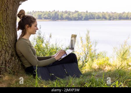 Lavora da qualsiasi luogo. Il freelance remoto lavora in natura. Giovane donna, freelancer femminile che lavora con un computer portatile con una bella vista di Foto Stock