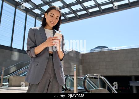 Sorridente giovane donna asiatica d'affari in piedi nella metropolitana della città usando il telefono. Foto Stock