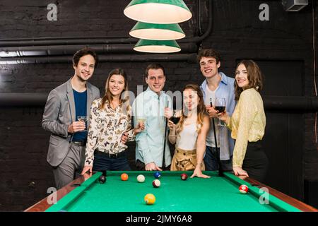 Gruppo felice sorridendo amici con bevande in piedi tavolo da biliardo Foto Stock