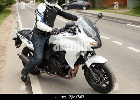 Il motociclista si porta su strada. Motociclista in pista. Motocicletta bianca. Dettagli del viaggio in casco. Foto Stock