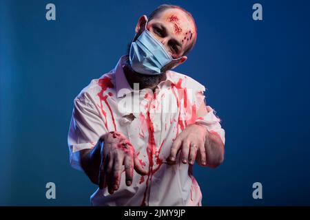 Cervello che mangia zombie in posa sulla macchina fotografica, guardando spaventoso e creepy con cicatrici e ferite sanguinose. Cadavere di Halloween non morto con aspetto pericoloso e viso ferito durante la pandemia del covid 19. Foto Stock