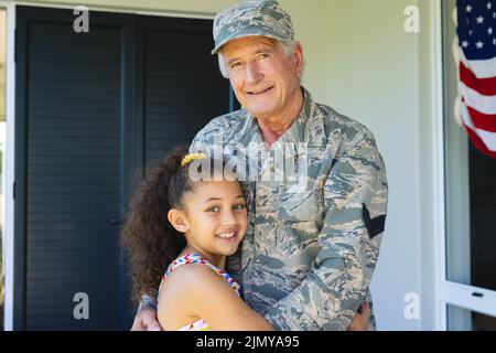 Ritratto di sorridente nonno militare multirazziale in abbigliamento camouflage abbracciando la nipote Foto Stock