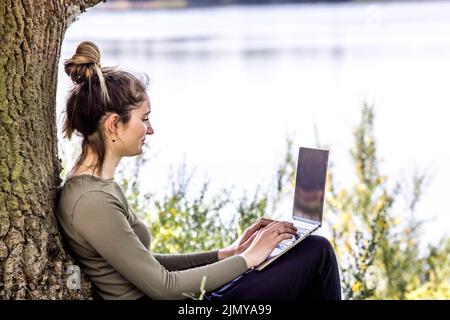 Lavora da qualsiasi luogo. Il freelance remoto lavora in natura utilizzando energia rinnovabile tramite un pannello solare pieghevole. Giovane donna, donna libera Foto Stock