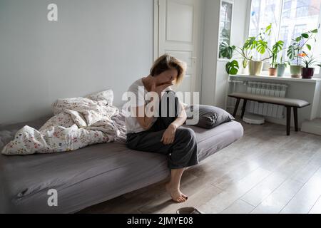La donna depressa di mezza età si siede sul letto scoperto che sbava dopo una sola notte insonne Foto Stock