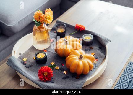 Autunno, autunno composizione accogliente umore per hygge home decor. Piccole zucche, candele e fiori di dahlia freschi sul vassoio con tovagliolo grigio sul Foto Stock