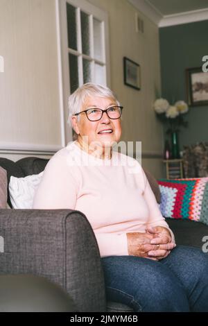 Ritratto di sorridente anziano, matura nonna in pensione in occhiali, anziana donna sorridente seduto sul divano a casa godendo la pensione. Scheda verticale Foto Stock