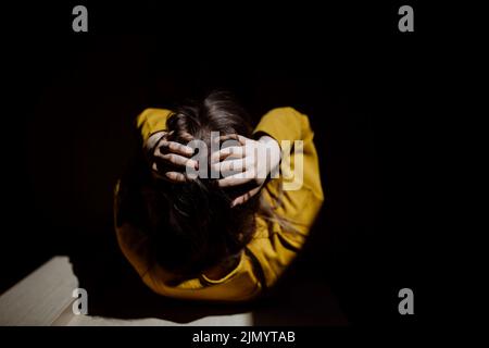 Vista dall'alto di una donna irriconoscibile che soffre di depressione e piange a casa, tenendo la testa nelle mani. Foto Stock