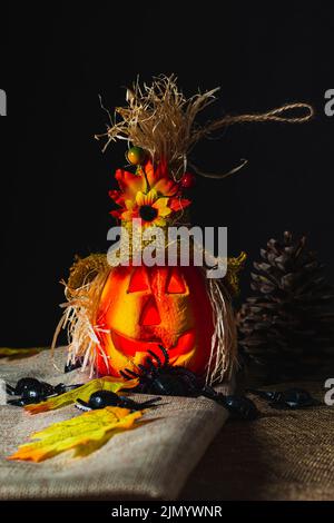 Zucca di Halloween decorata e illuminata all'interno, su sackcloth e circondata da ragni giocattolo e foglie cadute accanto ai coni di pino. Foto Stock