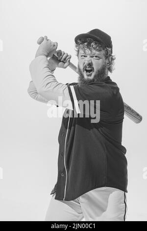 Ritratto monocromatico di giocatore di baseball maschile indossando una divisa sportiva retrò e tenendo la mazza isolata su sfondo bianco. Batteria da baseball d'epoca Foto Stock