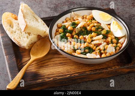 Stufato di ceci con spinaci e merluzzo o potaje de vigilia primo piano in una ciotola sul vassoio di legno sul tavolo. Orizzontale Foto Stock