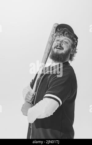 Ritratto monocromatico di giocatore di baseball maschile indossando una divisa sportiva retrò e tenendo la mazza isolata su sfondo bianco. Batteria da baseball d'epoca Foto Stock