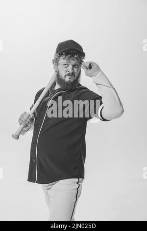 Ritratto monocromatico di giocatore di baseball maschile indossando una divisa sportiva retrò e tenendo la mazza isolata su sfondo bianco. Batteria da baseball d'epoca Foto Stock