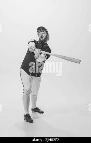 Ritratto monocromatico di giocatore di baseball maschile indossando una divisa sportiva retrò e tenendo la mazza isolata su sfondo bianco. Batteria da baseball d'epoca Foto Stock