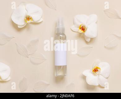 Un flacone dispenser per pompette vicino a fiori bianchi di orchidee con vista dall'alto in giallo chiaro, mockup. Pacchetto di prodotti per la cura della pelle. Cosmetici naturali esotici, pasta Foto Stock